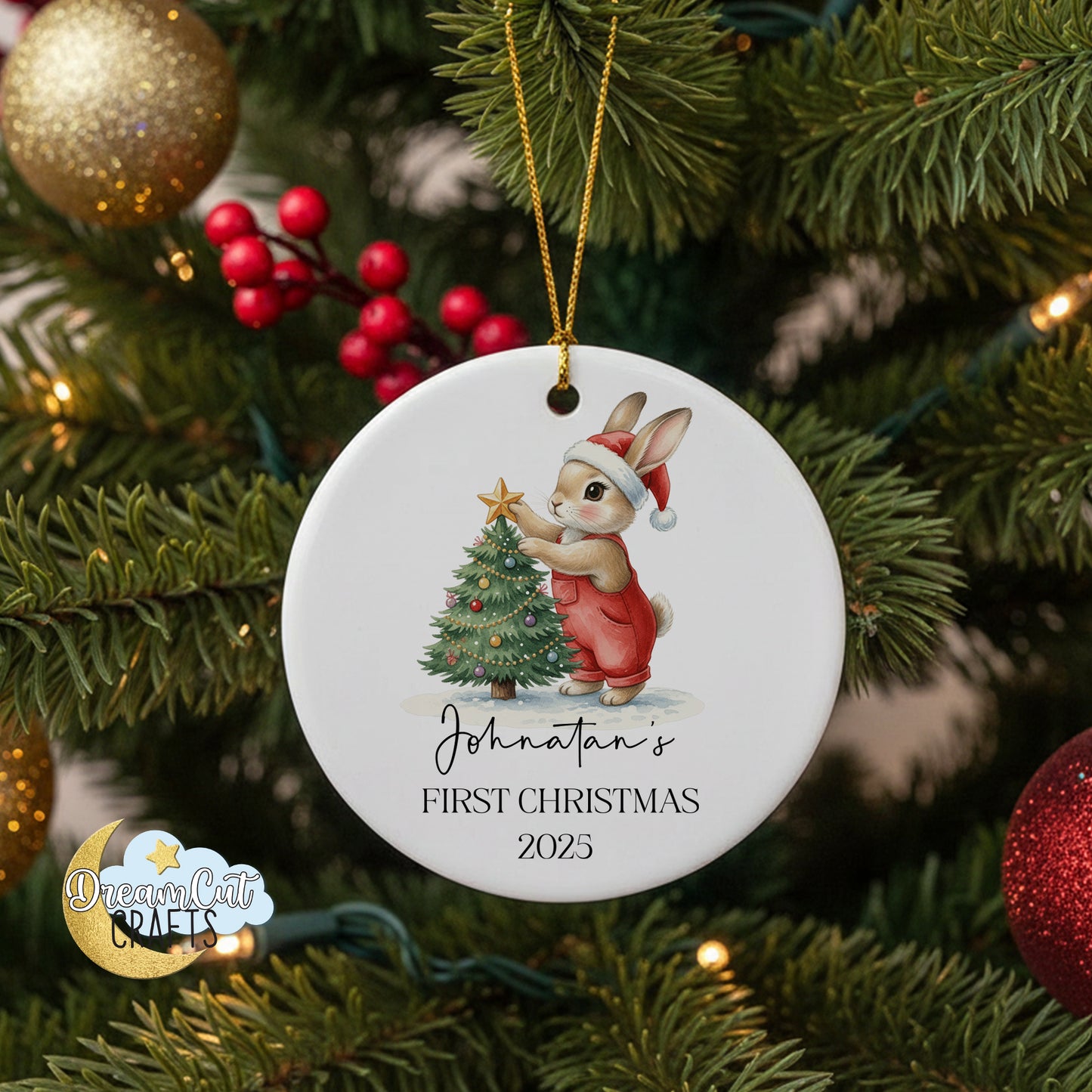 Round ceramic Christmas ornament with bunny in Santa hat placing a star on a decorated tree, personalized with name and year for baby’s first Christmas.