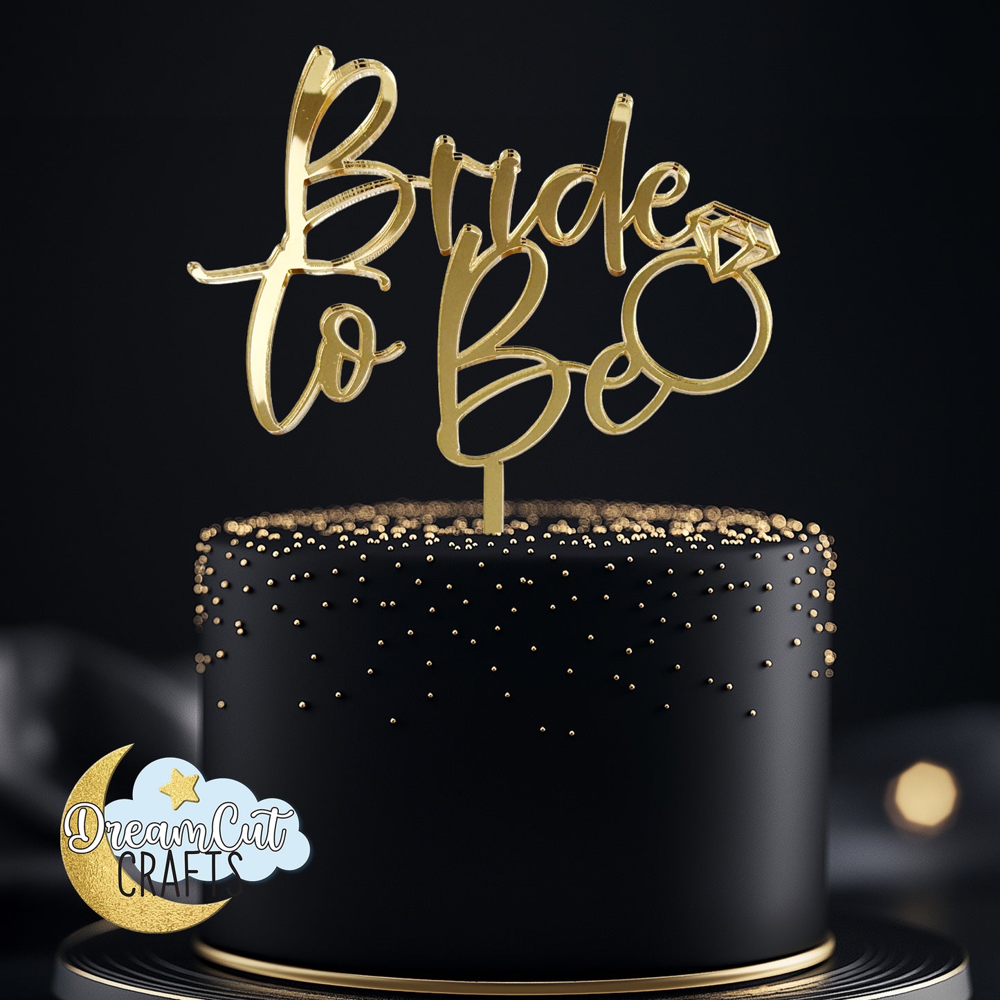 Gold mirror acrylic Bride to Be cake topper with script lettering and engagement ring detail displayed on an elegant black celebration cake.