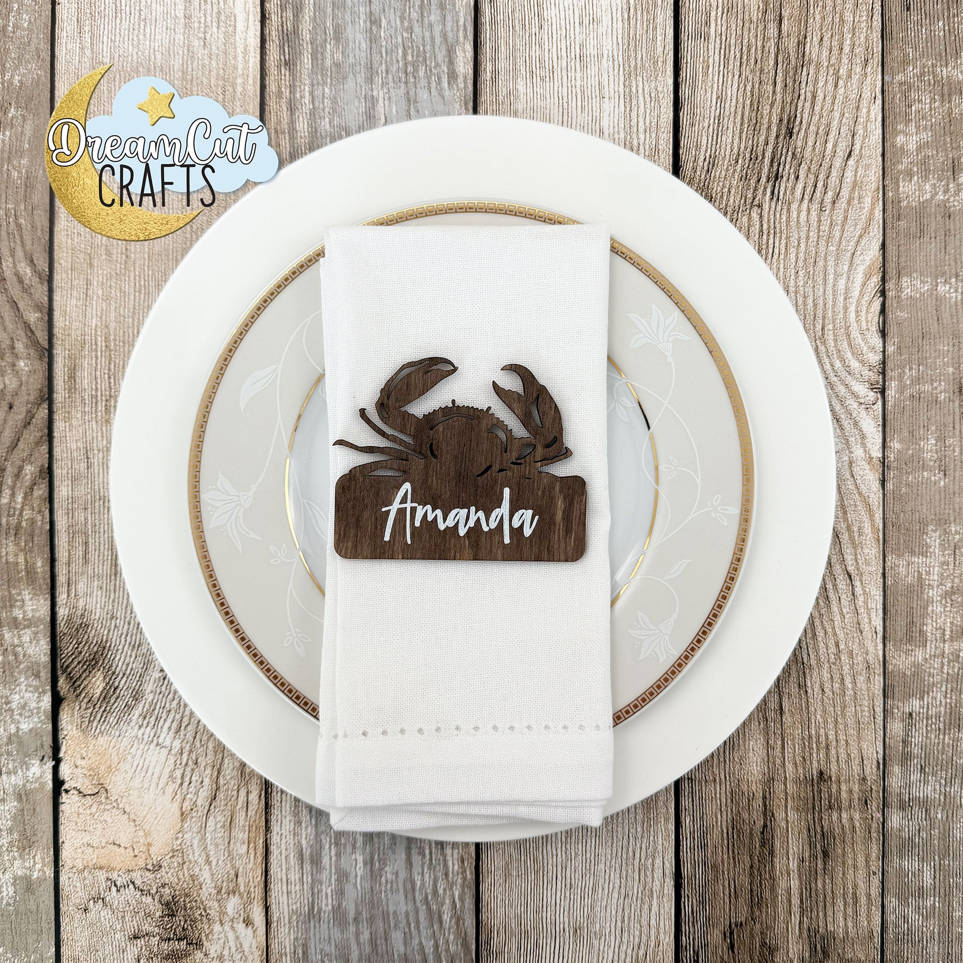 Wooden crab-shaped place card with custom name on a white napkin over a white plate.