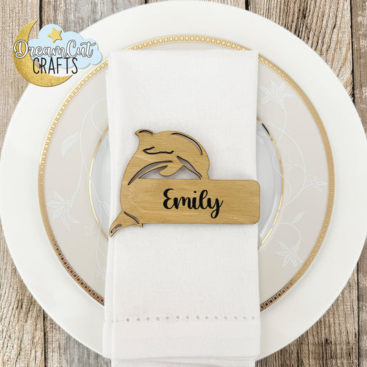 Wooden wedding place card with a custom name engraved on a white napkin over a white plate.