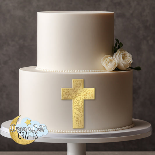 Gold acrylic cross cake charm with engraved scroll details attached to the front of a white baptism cake