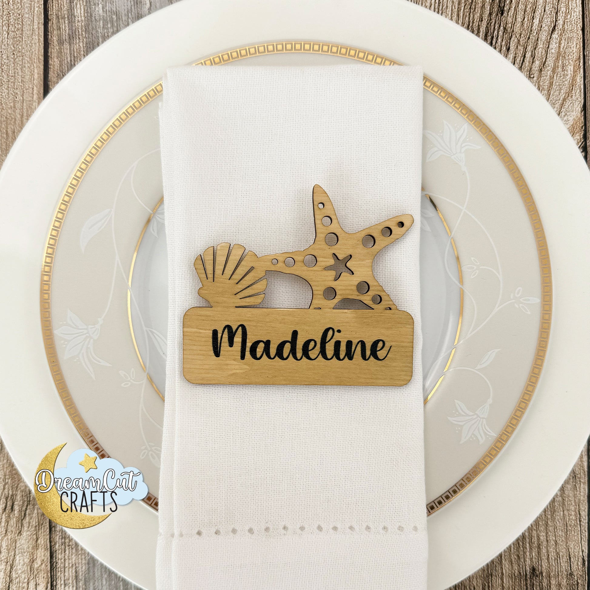 Wooden wedding place card with starfish and shell design on a white napkin over a decorative plate.
