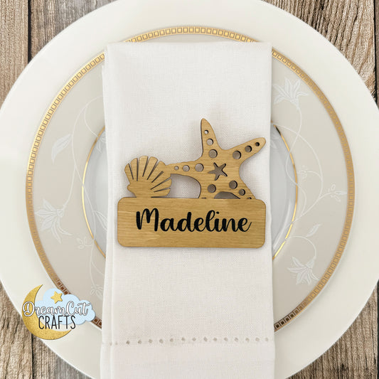 Wooden wedding place card with starfish and shell design on a white napkin over a decorative plate.