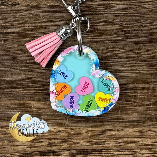 Personalized heart shaker keychain with turquoise acrylic base, colorful mini hearts inside, pink tassel, and custom name on the back